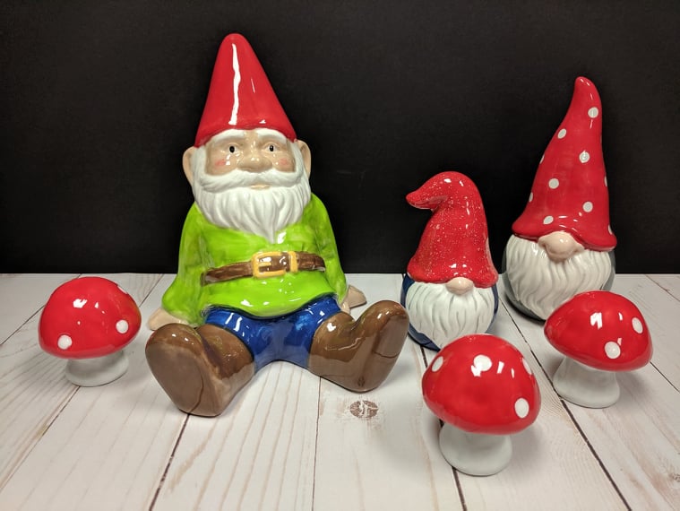 A gnome sitting on the ground next to some mushrooms.