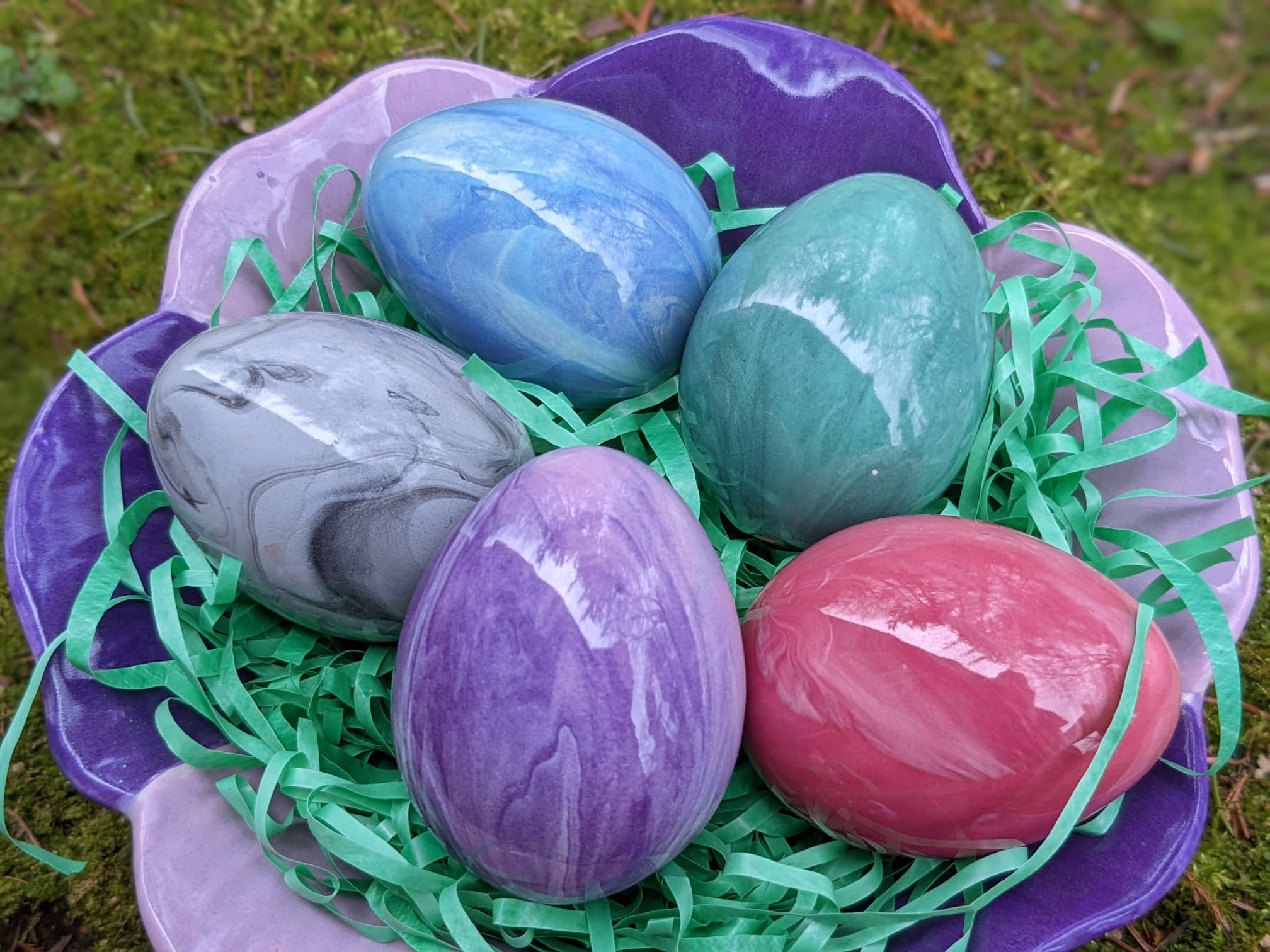 A basket of colored eggs sitting on top of grass.