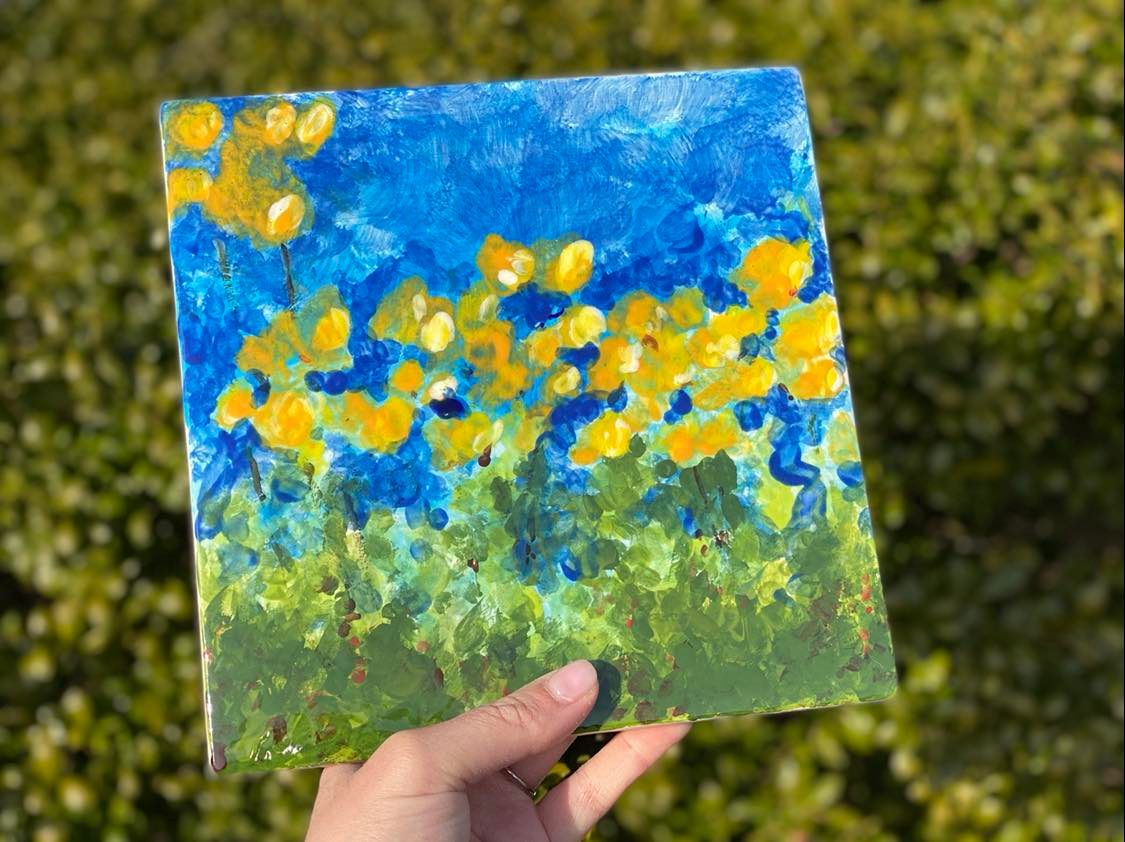 A hand holding up a painting of yellow flowers.