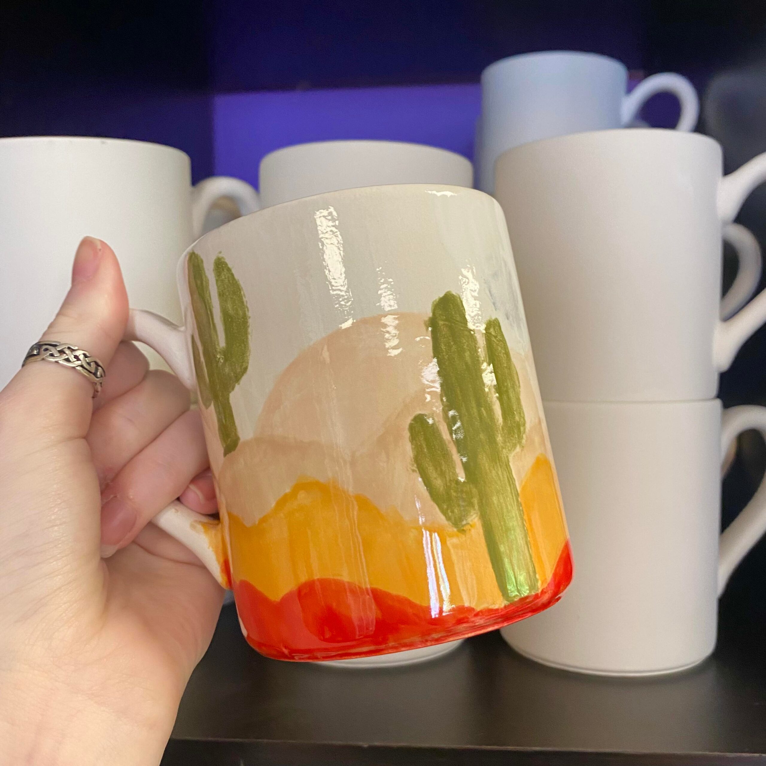 A hand holding a coffee mug with cactus on it.