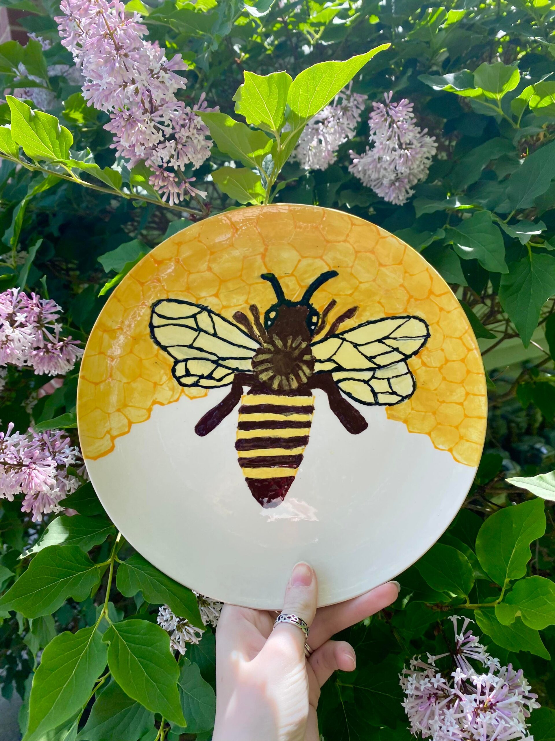 A hand holding up a plate with a bee on it.