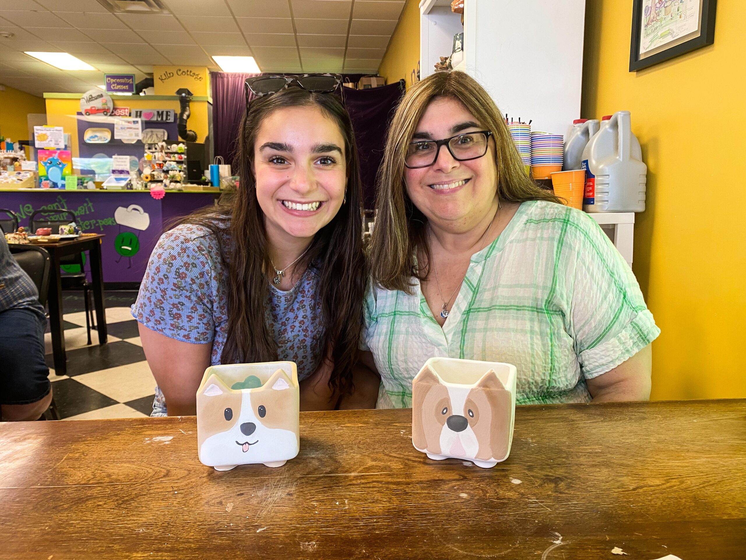 Two women sitting at a table with paper mache dog boxes.