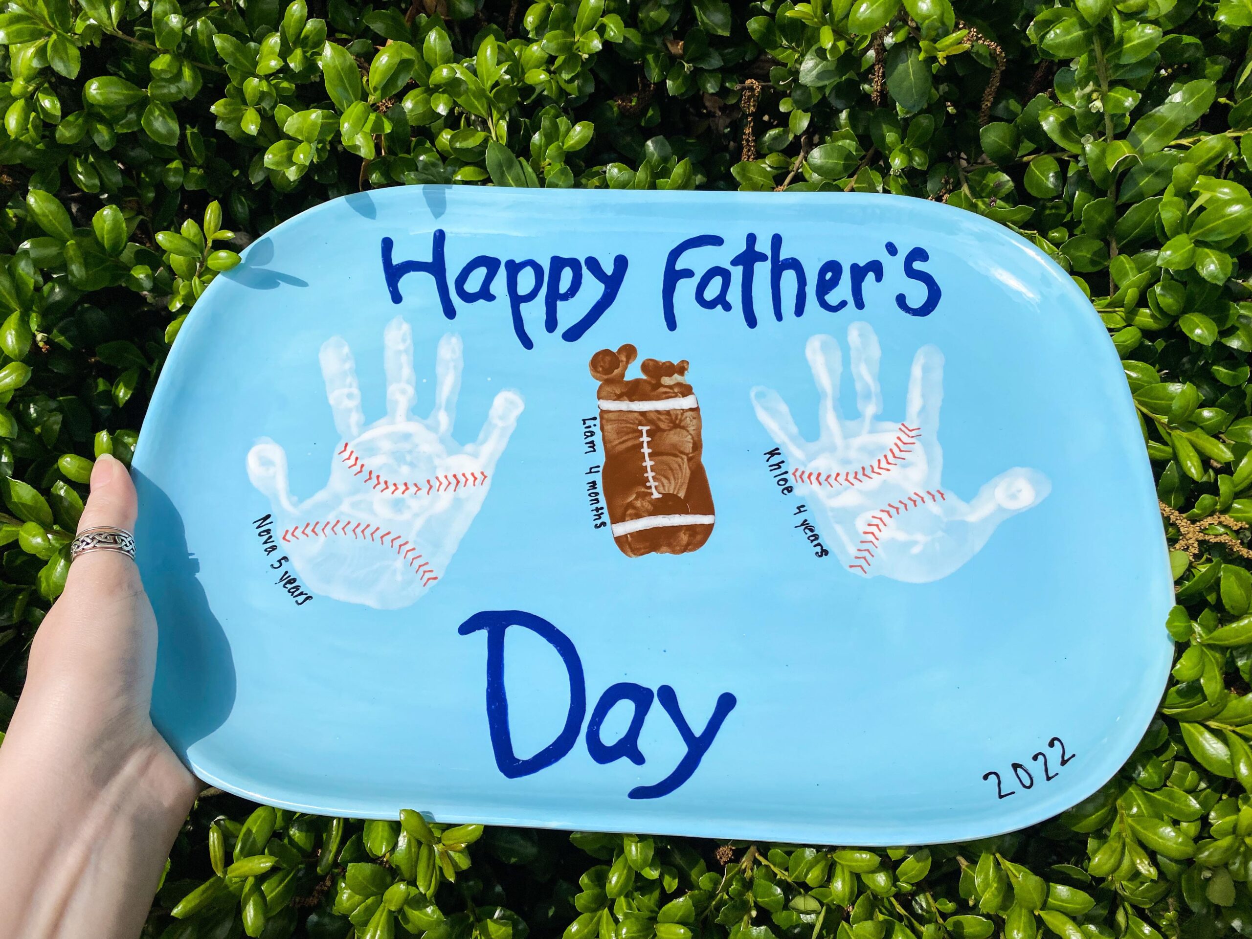 A blue tray with handprints and baseball mitt on it.