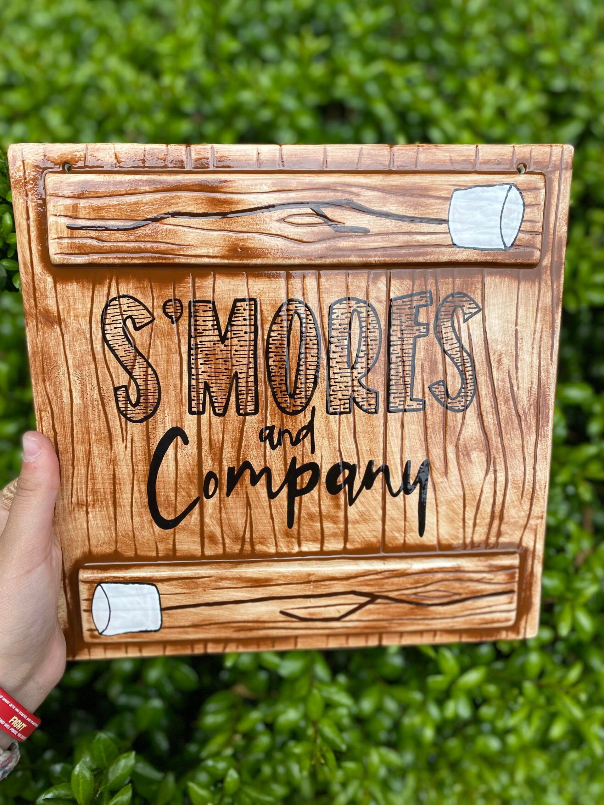 A hand holding up a wooden box with the words " s 'm ores and company ".