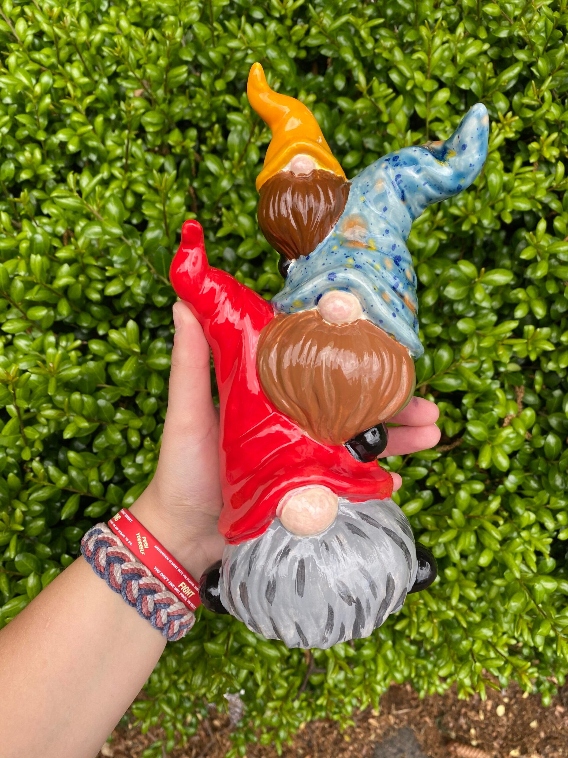 A hand holding two gnomes in the grass.