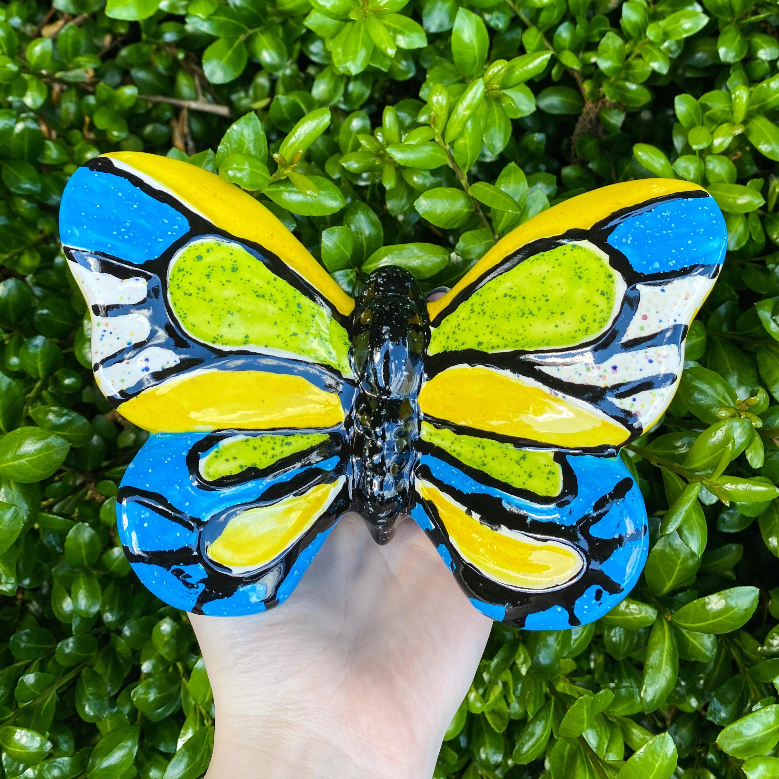 A hand holding up a butterfly with blue and yellow wings.