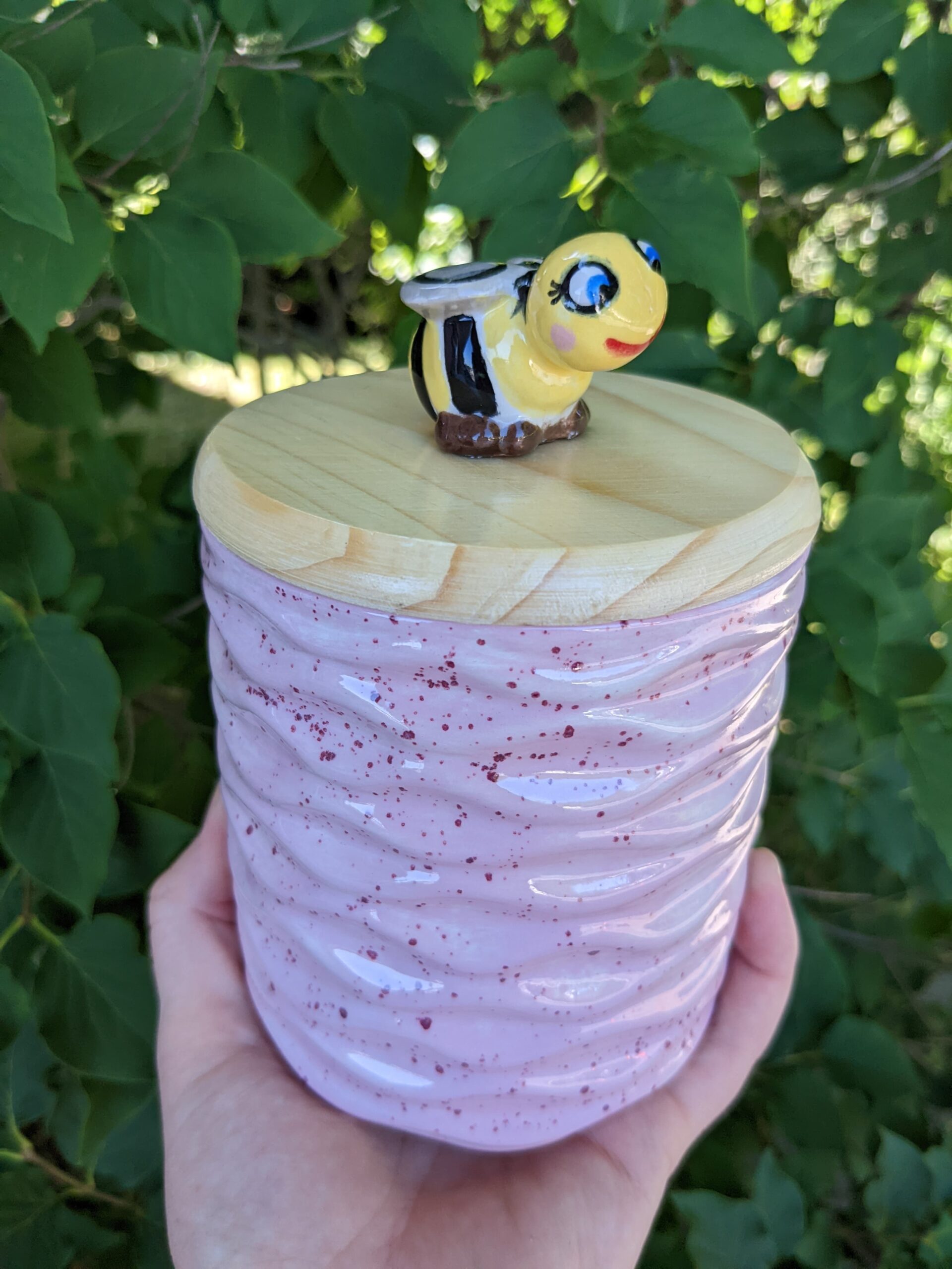 A person holding a pink container with a bee on top of it.