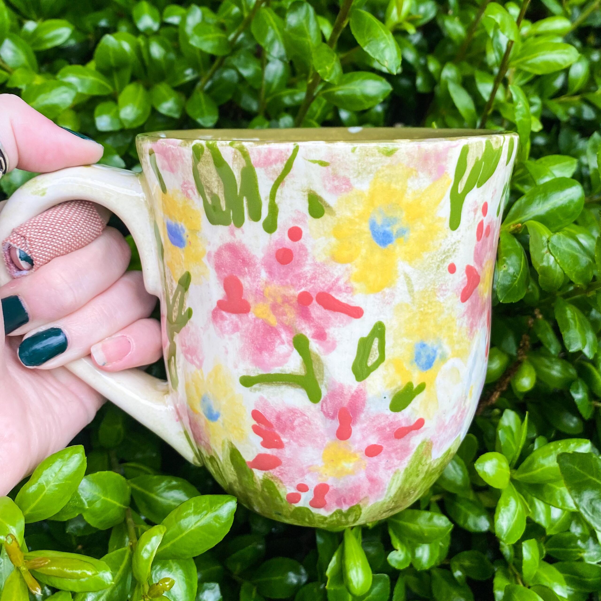 A hand holding a coffee mug in the grass.