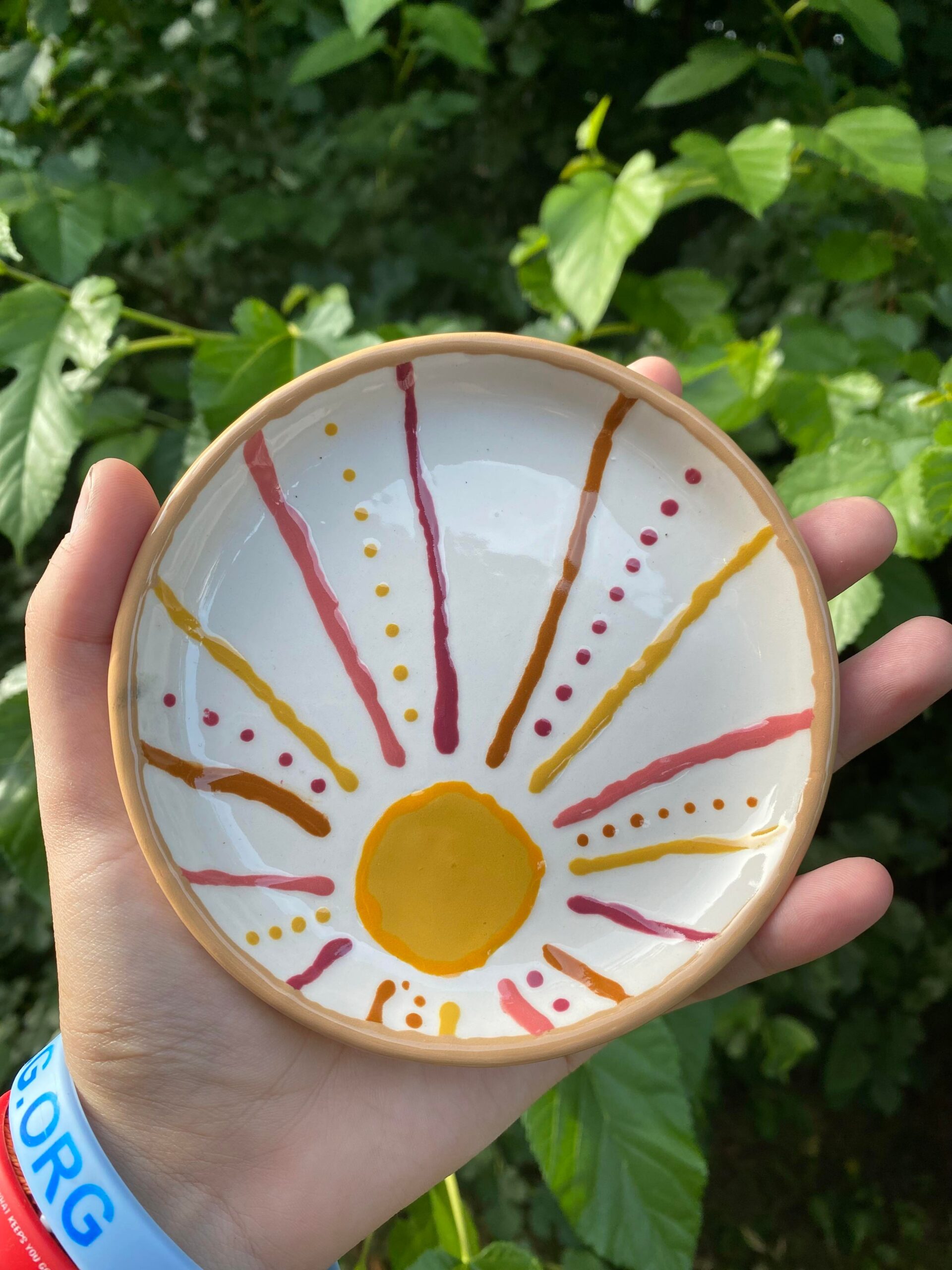 A hand holding a bowl with an orange sun design on it.
