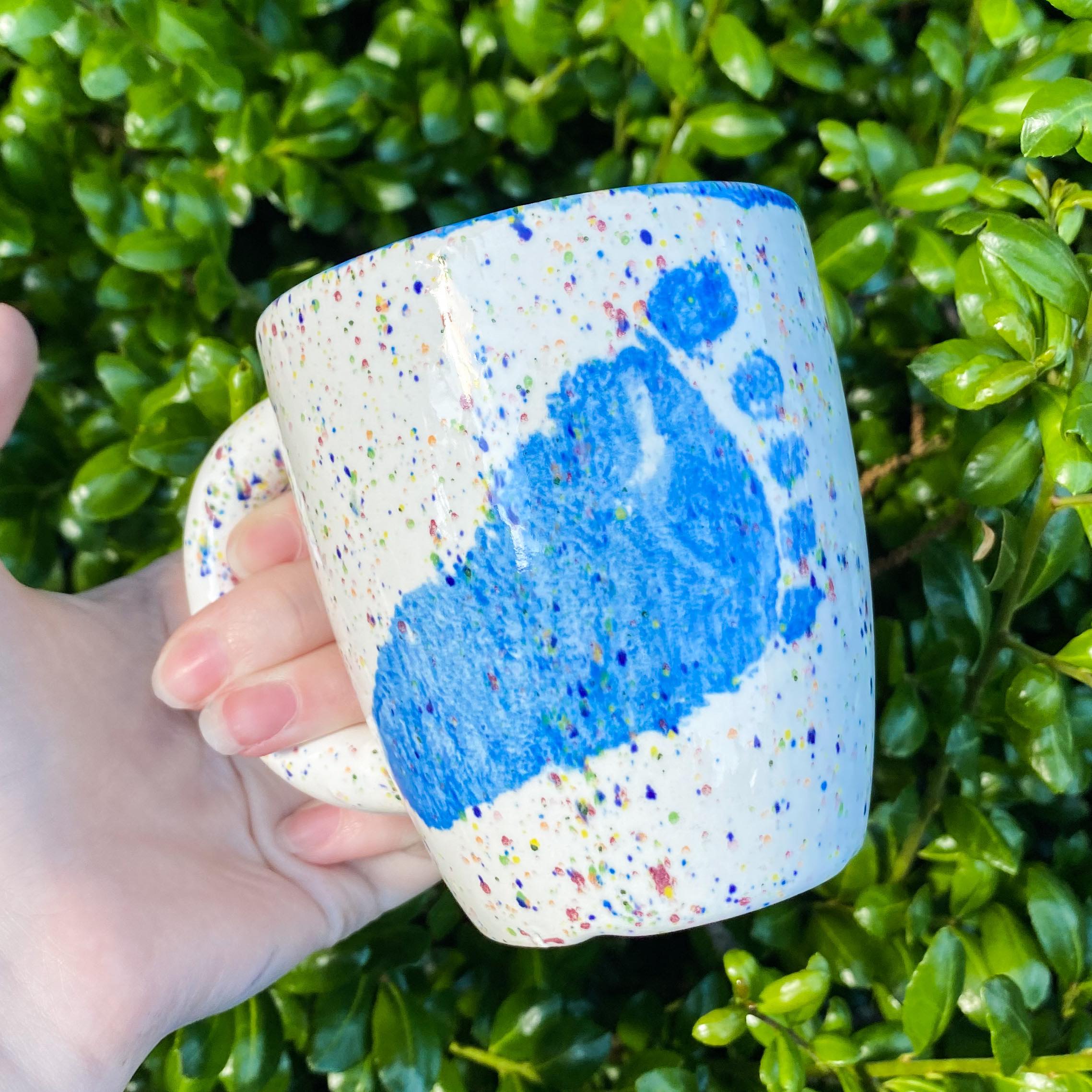A person holding a coffee mug with blue paint on it.