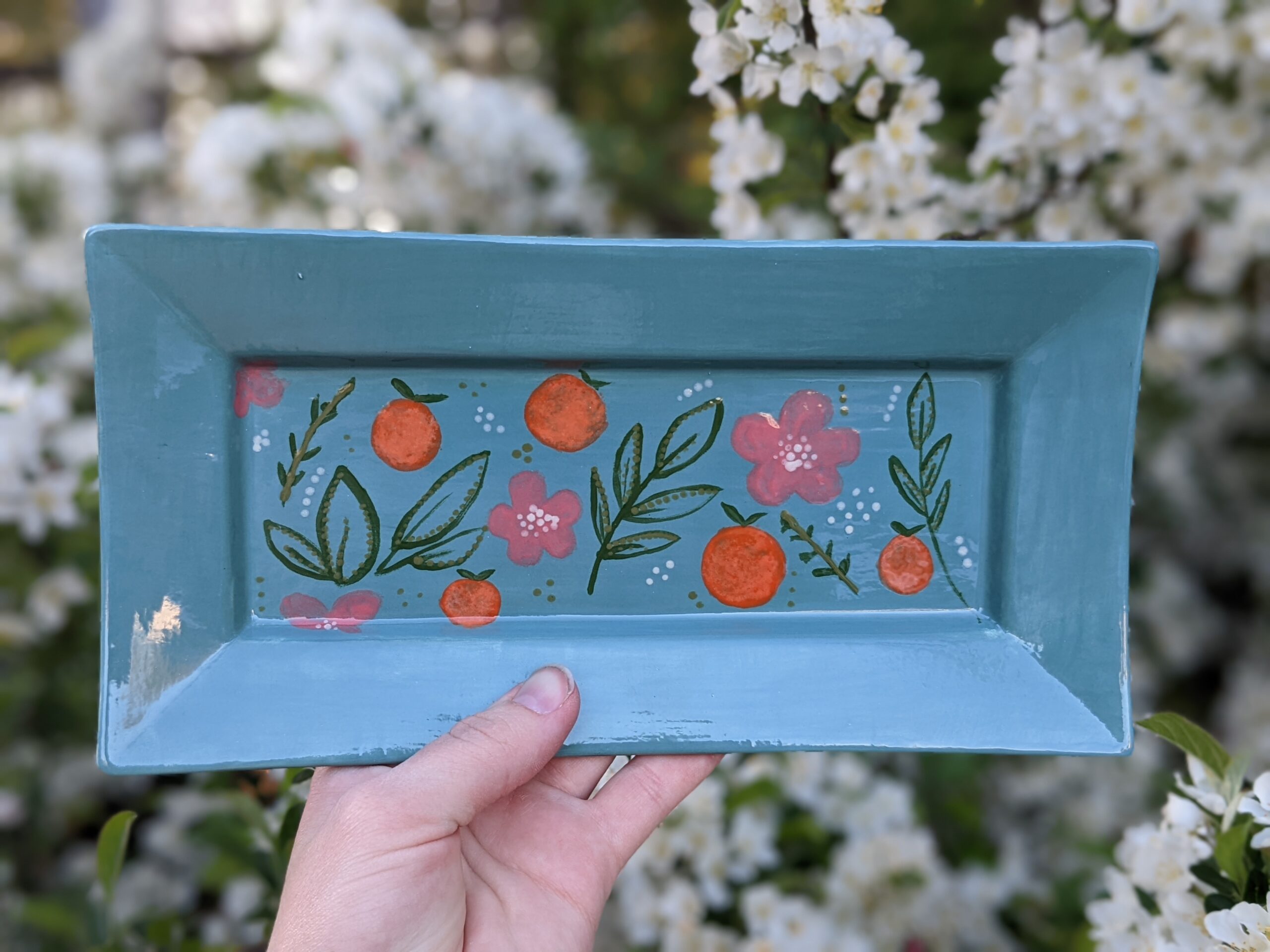 A hand holding an empty blue tray with orange and pink flowers.