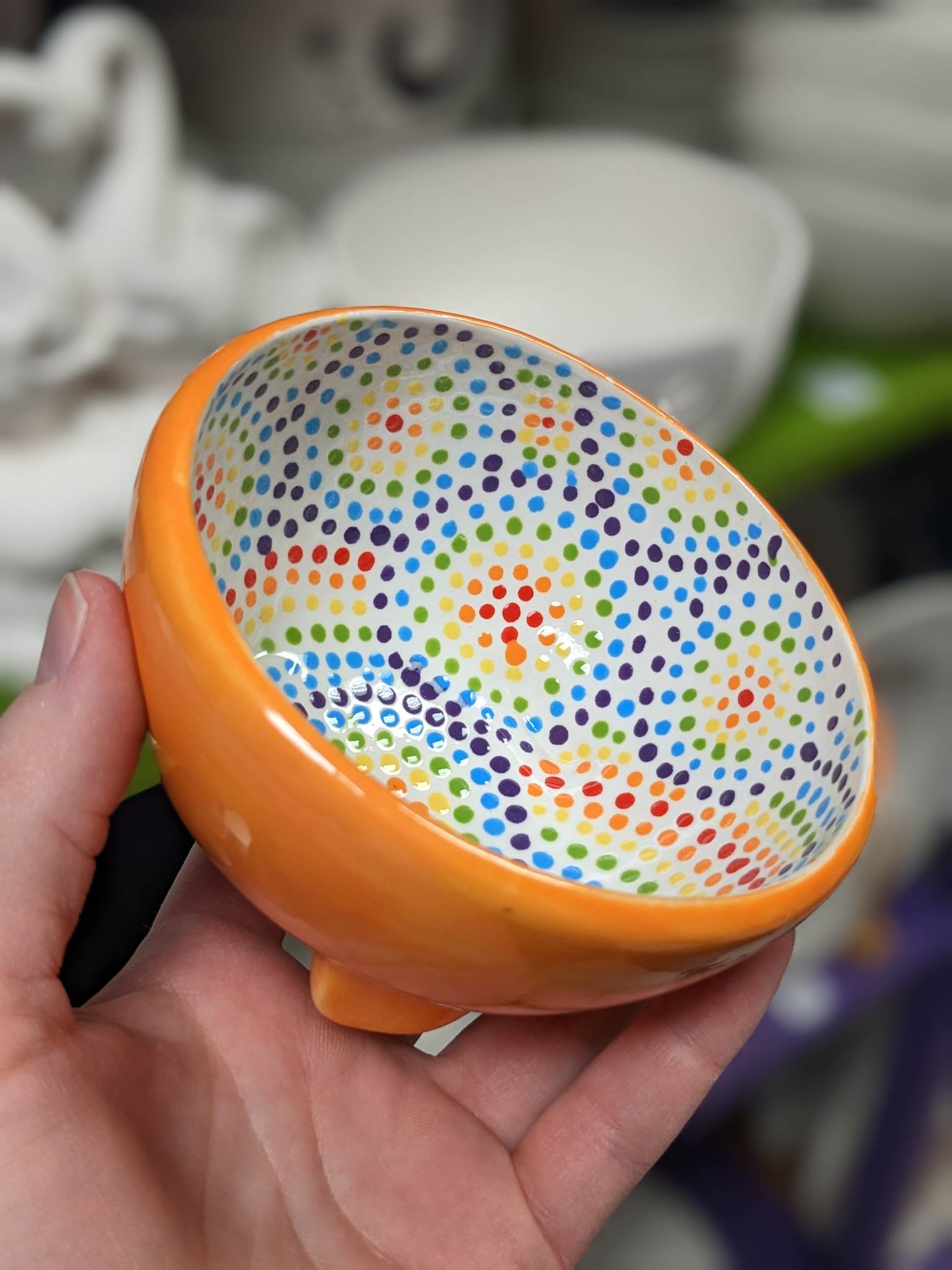 A person holding an orange bowl with colorful dots on it.