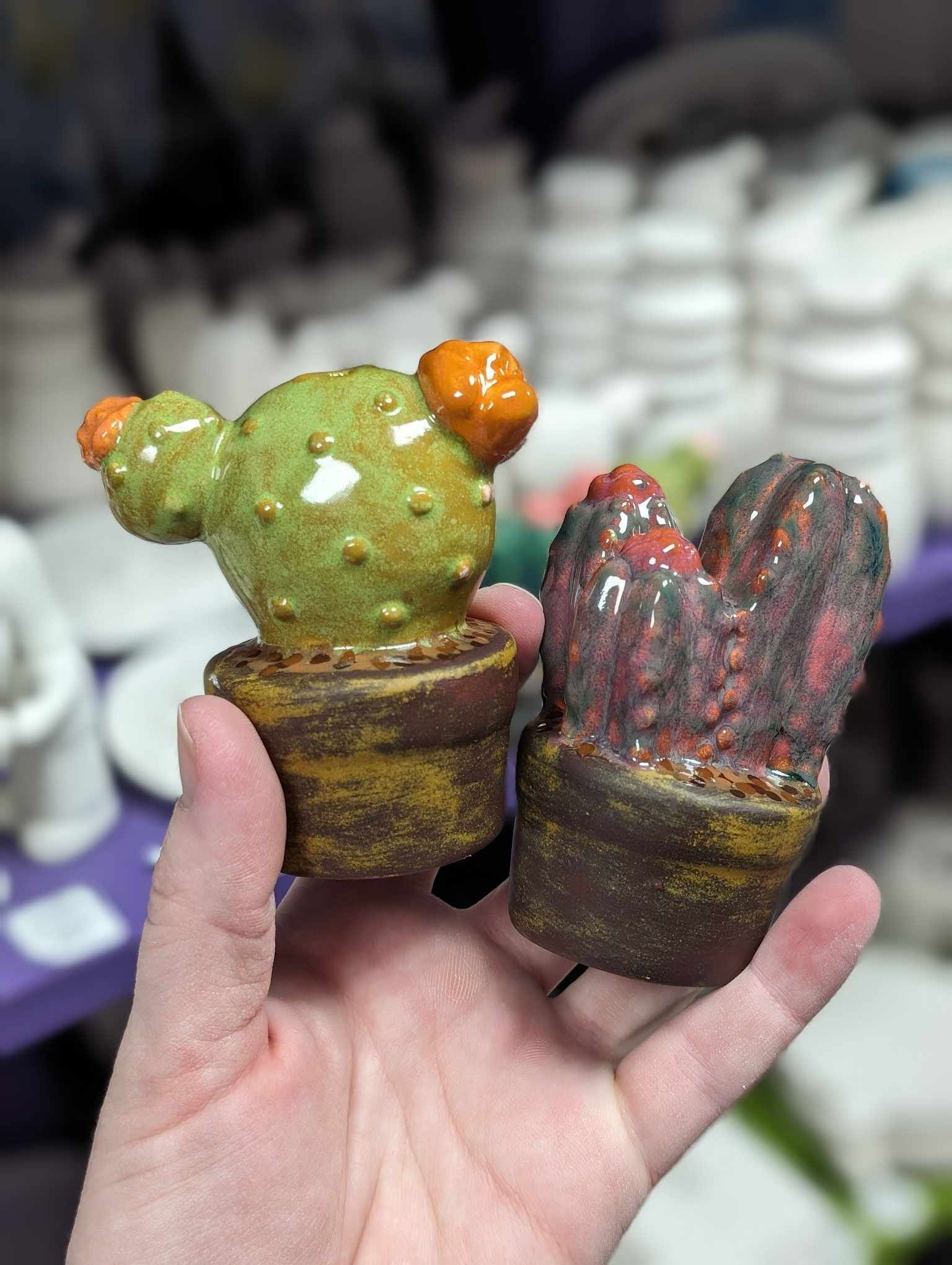 A person holding two ceramic cacti in their hand.